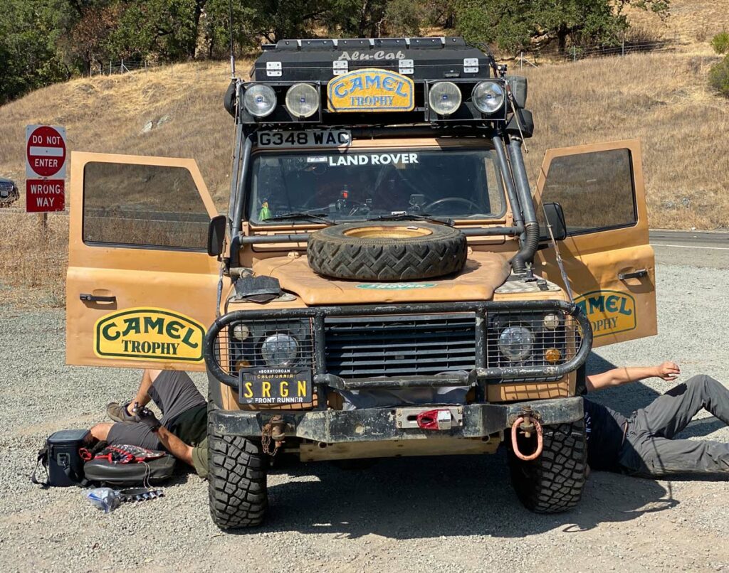 Two people under an overland truck fixing it